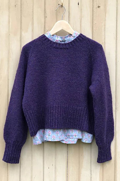 A purple sweater with long sleeves hangs against a wooden wall