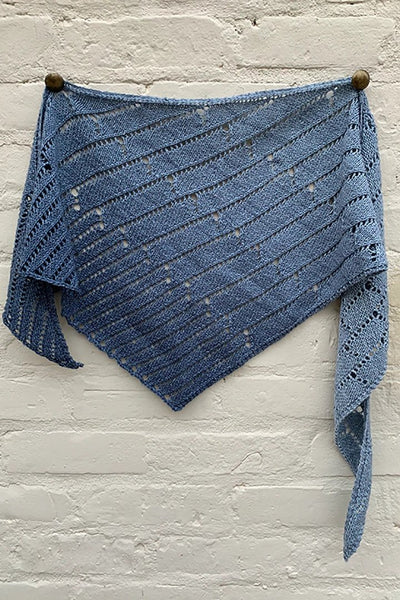 A blue grey shawl hangs on a white brick wall