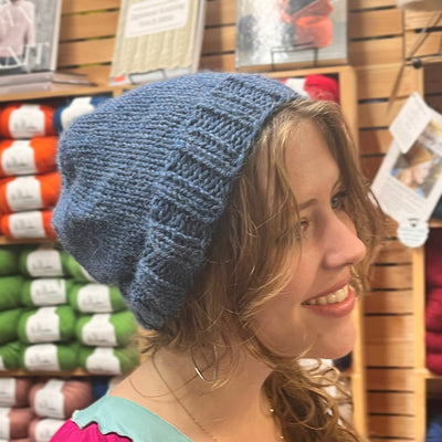 A blond woman with red lipstick wears a caramel colored knitted beanie
