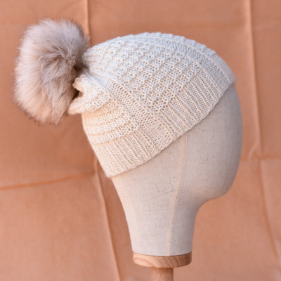 a cream knitted hat with furry pom pom