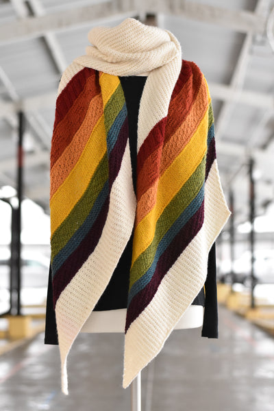 A cream knitted wrap with rainbow stripes at each end