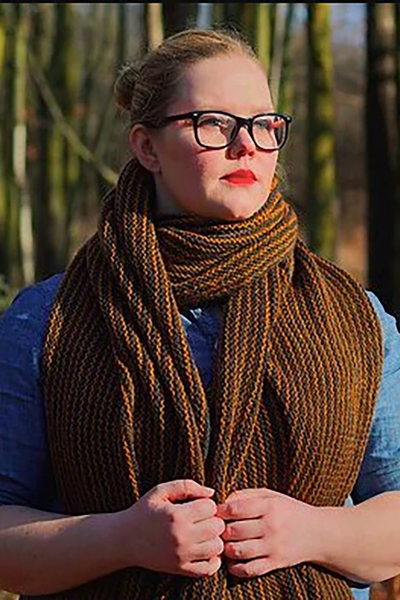 A blond woman with glasses and red lipstick wears a brown and black striped shawl