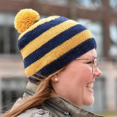 two navy blue and gold striped beanies with pom poms
