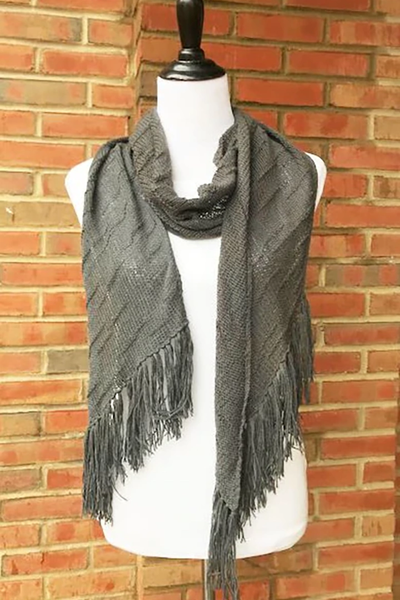A dark grey fringed knit scarf in front of a brick wall