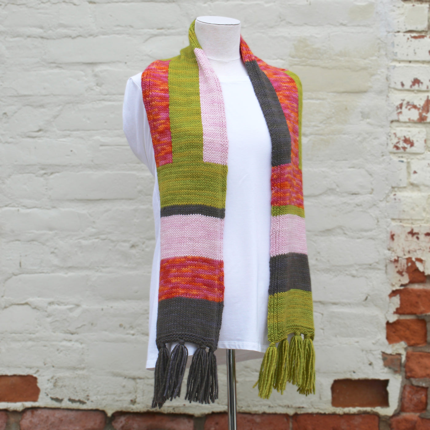 Colorful striped scarf with tassels on a mannequin against a brick wall.